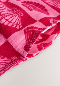Tissu rouge et rose avec des motifs alternés d'ailes de papillon en damier, montrant un tissage texturé et un bord plié.