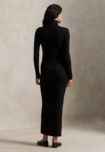 Μαύρο ριμπ πλεκτό φόρεμα με ρόμβους, μακρυμάνικο, εφαρμοστή σιλουέτα, μήκος μέχρι τους αστραγάλους, απαλό ύφασμα, συνδυασμένο με μαύρα φλατ παπούτσια.