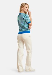 Gebreid T-shirt met korte mouwen in blauwe en groene strepen, met een effen blauwe zoom. Gecombineerd met crèmekleurige, rechte broek en casual schoenen.