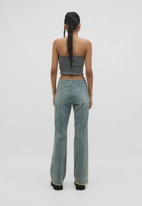 Top corto de canalé gris combinado con jeans de pierna ancha azul claro, con dobladillos deshilachados. Modelo de espaldas, mostrando el diseño trasero.