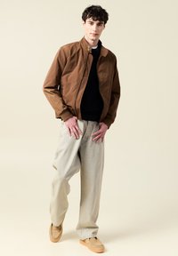 Brun lätt bomberjacka med dragkedja fram, ihop med ljusgrå vida byxor och beigea slip-on skor. Slät textur, avslappnad passform.