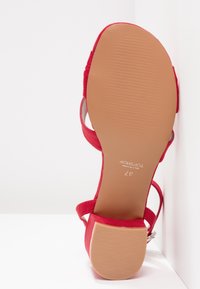 Sandale à talon haut en daim rouge avec plusieurs brides et une semelle en caoutchouc texturé beige. Taille 37 indiquée sur le pied.