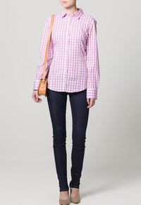 Rosa och vit rutmönstrad skjorta med knappar och långa ärmar, tillsammans med mörka skinny jeans och en ljusbrun axelväska.