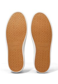 Calvin Klein sneakers med gummisåler, der har en tan tekstureret overflade, prægede logoer og hvid kant omkring sålen.