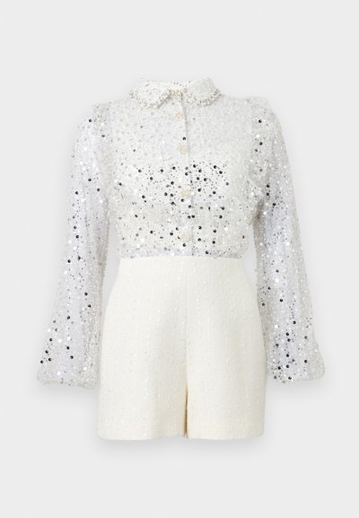 Blouse blanche à manches longues à sequins, boutonnée avec col, associée à un short blanc texturé taille haute, sur fond sans détails.
