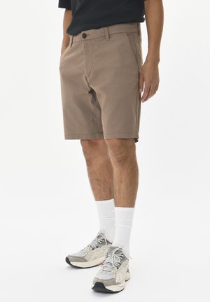Brown cotton shorts with a relaxed fit, side pockets, and a button closure. Worn with grey sneakers and white ankle socks.