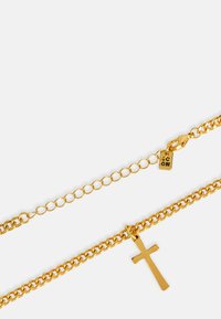 Arany színű fém nyaklánc, váltakozó láncszemekből álló lánc dizájnnal, fényes kereszt medállal díszítve. Kapcsok és címkék láthatók.
