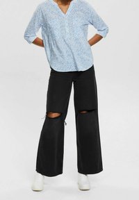 Hellbluse mit Muster und V-Ausschnitt, dreiviertel Ärmeln, kombiniert mit schwarzen weit geschnittenen Jeans mit Knieverletzungen und weißen Sneakers.
