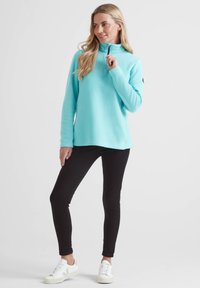 Light blue fleece pullover with half zipper, long sleeves, and side vents, paired with black leggings and white sneakers.
