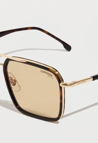 Gafas de sol de carey con un marco de metal dorado y lentes de color marrón. Incluye una marca grabada en las patillas y almohadillas ajustables en la nariz.