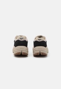 Apsuktas sneakers modelis, kuriame dominuoja juodos, smėlio ir rožinės spalvos derinys, pagaminti iš zomšos ir tinklinio medžiagų, su tvirtu guminuku ir prekės ženklo logotipu.