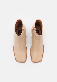 Beżowe skórzane botki za kostkę z kwadratowym noskiem, bocznym zamkiem i jasnobrązowymi przeszyciami; gładka faktura i minimalistyczny design.