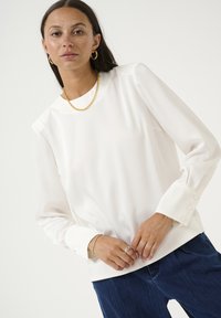 Witte blouse met lange mouwen in een textuurstof, met een ronde halslijn, knoopmanchetten en een ontspannen pasvorm, gecombineerd met donkerblauwe broek.