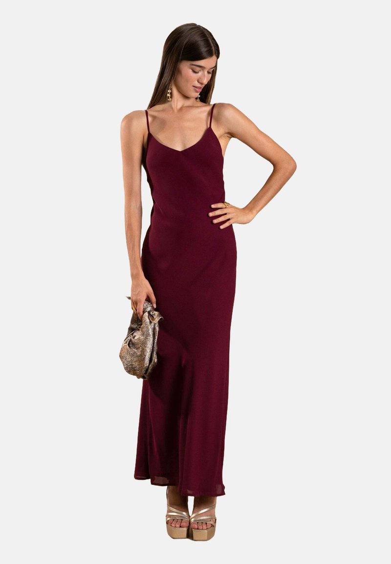 Burgunderfarbnes ärmelloses Kleid mit gerader Silhouette, weichem Stoff und bodenlanger Saumlinie. Kombiniert mit einer metallischen Tasche und Plateauschuhen.