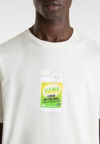 Valkoinen puuvillapaita, jossa on vihreä ja keltainen grafiikka puhdistusainepullosta, jossa lukee "VANS LIQUID OFF THE WALL".
