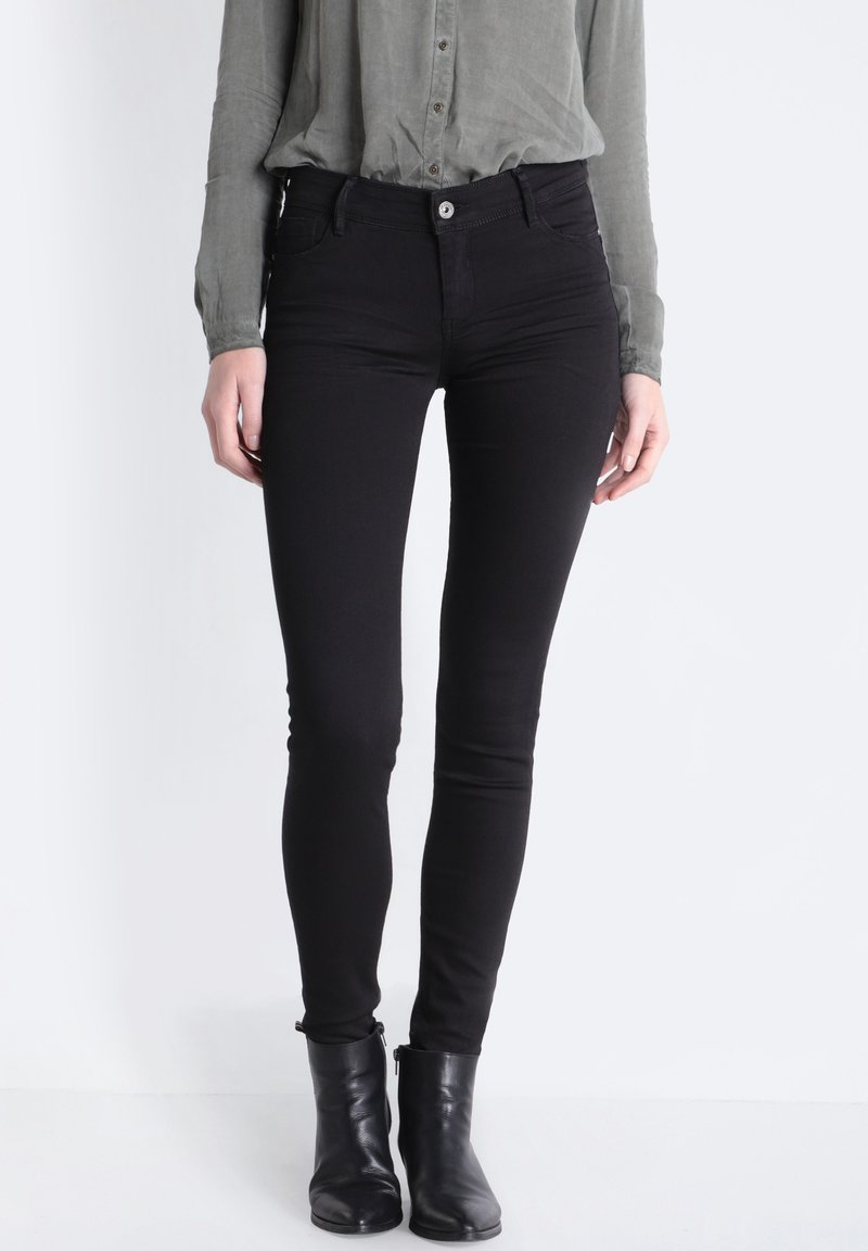 Czarne wąskie dżinsy wykonane z denimu, z średnim stanem, subtelnym przeszyciem i zapięciem na guzik z przodu, w połączeniu z czarnymi botkami za kostkę.