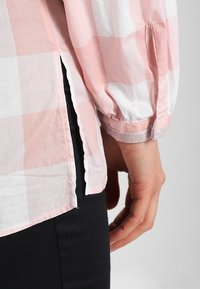 Camisa de manga larga a cuadros rosa claro y blanca con puños elásticos, aberturas laterales y una tela ligera y texturizada.