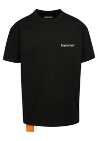 Svart bomull T-skjorte med rund hals, korte ermer, og en liten hvit "glemte ansikter" logo. Har et oransje merket på kanten.