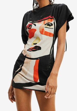 Femme portant une robe noire à manches courtes avec un grand motif abstrait de visage en rouge, blanc, jaune et noir sur le devant.