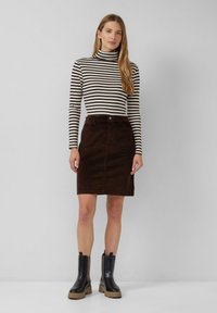 Gestreepte coltrui, bruine corduroy rok, knie-lang. Zwarte enkellaarsjes met dikke zolen en zij-elastische panelen. Effen grijze achtergrond.