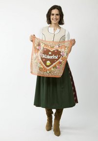 Herzförmiger Oktoberfest-Dekorationsstoff mit bunten Blumenmustern und weißem Schriftzug, gehalten von einer Person in traditioneller Tracht.