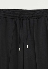 Ceinture à cordon noir de pantalon en tissu texturé avec deux cordons suspendus munis de pointes en métal.