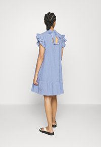 Robe rayée bleu et blanc avec manches à volants, lien au dos du cou, et ourlet évasé. Tissu léger et coupe mi-longue.