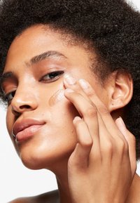 Siero viso trasparente applicato sulla pelle, che mostra una consistenza liscia e leggera. Il soggetto ha capelli ricci, un incarnato naturale e un colore labbra neutro.