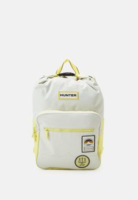 Ljust grå och gul ryggsäck med dragsnörning i toppen och framficka med dragkedja, prydd med varumärket "HUNTER" och dekorativa lappar.