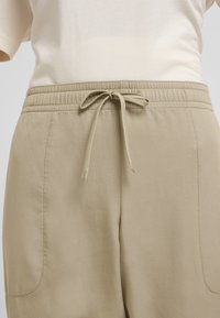 Beige elastische tailleband broek met een trekkoord, voorzien van zijzakken en een gladde, geweven textuur. Casual en comfortabel ontwerp.