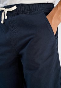 Granatowe szorty wykonane z lekkiego materiału, z elastycznym paskiem na talii i sznurkiem do regulacji. Posiadają boczne kieszenie oraz widoczne przeszycia.