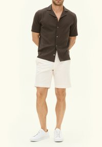 Short-sleeved brown textured shirt with buttons, paired with white shorts and white sneakers. Simple design with a collar.