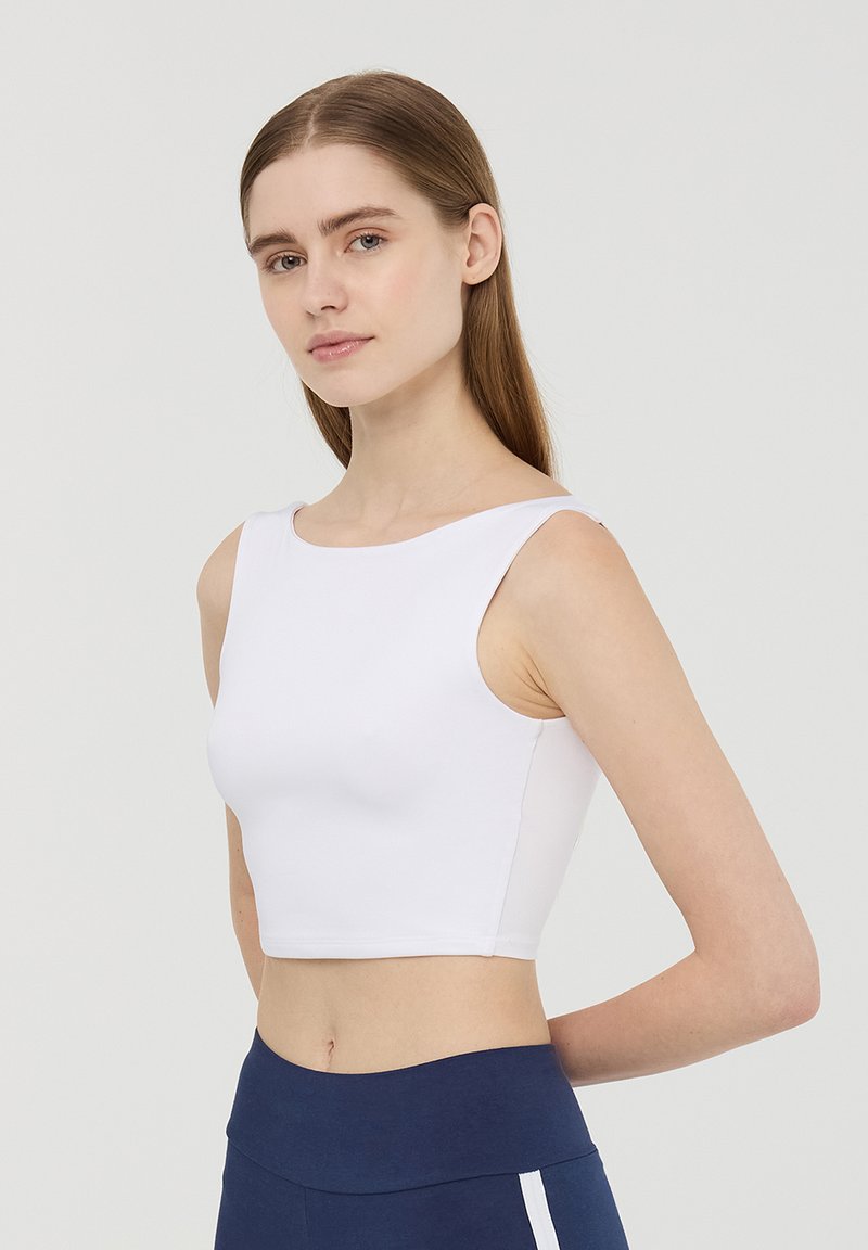 Top corto bianco con ampie armature e scollatura rotonda, realizzato in un materiale liscio e elasticizzato, abbinato a leggings sportivi blu navy.