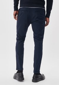 Granatowe chinosy o slim fit, z bocznymi kieszeniami, dwiema tylkami z guzikami i podwiniętymi mankietami. Gładka faktura materiału.