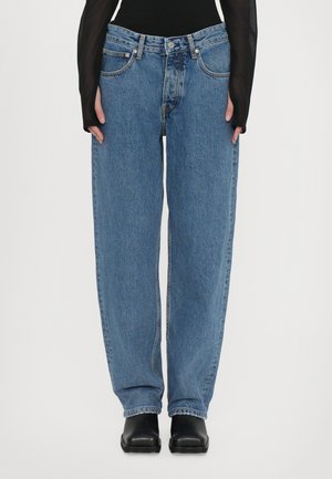Hochgeschnittene blaue Denim-Jeans mit lockerer Passform, fünf Taschen, subtiler Ausbleichung und geradem Bein. Sichtbare schwarze Ankle-Boots.