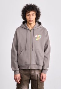 Gray zip-up hoodie made of cotton blend with a front pocket and multicolored "NIKE SB" logo. Features a drawstring hood and ribbed cuffs.