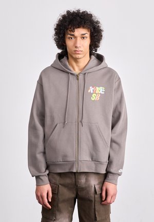 Gray zip-up hoodie made of cotton blend with a front pocket and multicolored "NIKE SB" logo. Features a drawstring hood and ribbed cuffs.