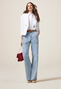 Blazer blanco, abotonado, con acentos dorados; camisa blanca; jeans de tiro alto azul claro con bolsillos con tachuelas; bolso rojo; tacones beige.