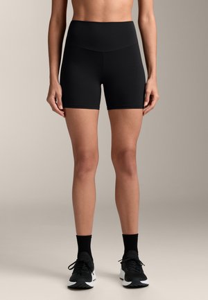Sorte høj taljerede shorts lavet af strækbart stof, med en glat talje og tætsiddende design, parret med sorte atletiske sko og sokker.