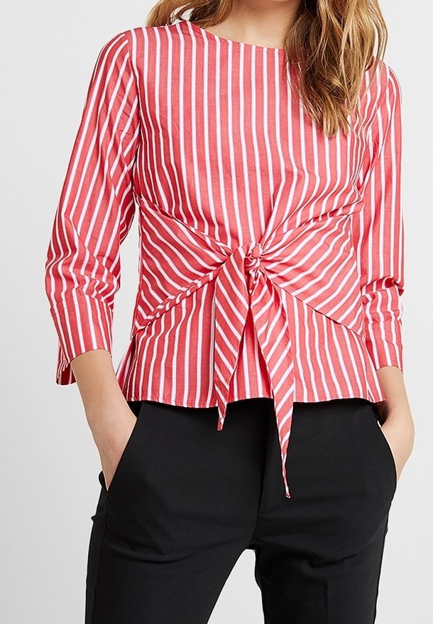 Maglietta a righe rosse e bianche con maniche lunghe e dettaglio ancorato davanti, realizzata in tessuto leggero, abbinata a pantaloni neri.