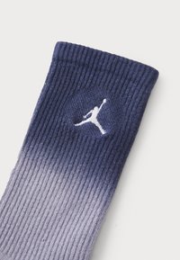 Șosetă de echipament cu gradient albastru, textură împăturită, având un logo Jumpman alb pe un fundal circular aproape de vârf. Design moale, athletic.