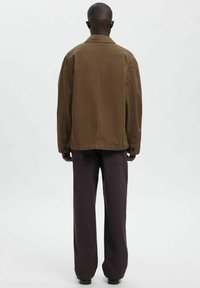 Brązowa kurtka z kołnierzem wykonana z gładkiej tkaniny, o prostym kroju. Połączona z szerokimi spodniami o ciemnofioletowym kolorze. Prosty, funkcjonalny design.
