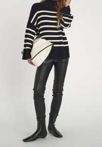 Sweter dzianinowy w czarno-białe paski, luźny krój, zestawiony z dopasowanymi czarnymi skórzanymi spodniami i czarnymi botkami na kostkę, trzymając beżową torebkę.