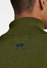 Grüner gerippter Rollkragenpullover mit strukturierter Oberfläche, versehen mit einem G-Star Originals Etikett auf der Rückseite.