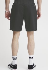 Shorts de sport noirs avec une taille élastique, associés à des chaussettes blanches montantes avec des rayures noires, portés avec des baskets noires.