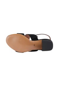 Sandal in suede nero con suola beige liscia, caratterizzata da un lieve tacco e un design aperto. La parte inferiore mostra un accentuato tacco in gomma nera testurizzata.