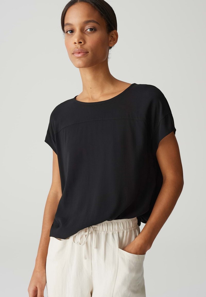 Zwarte korte mouwen top met een ronde halslijn en subtiele naden, gecombineerd met lichte, loszittende broek met zakken.