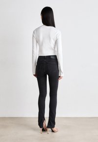 Fekete skinny farmernadrág magas derékkal, hátsó zsebekkel és sötét szövettextúrával. Hosszú ujjú fehér felsővel és bézs magassarkúval párosítva.