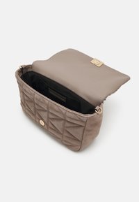 Sac à main matelassé taupe avec rabat ouvert révélant une doublure intérieure noire et une fermeture ainsi que des anneaux métalliques dorés sur les côtés.