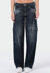 Donkerblauwe wijdetopje jeans met een vervaagde textuur, voorzakken en contrasterende stiksels. Draag ze met witte sneakers, wat de casual uitstraling benadrukt.